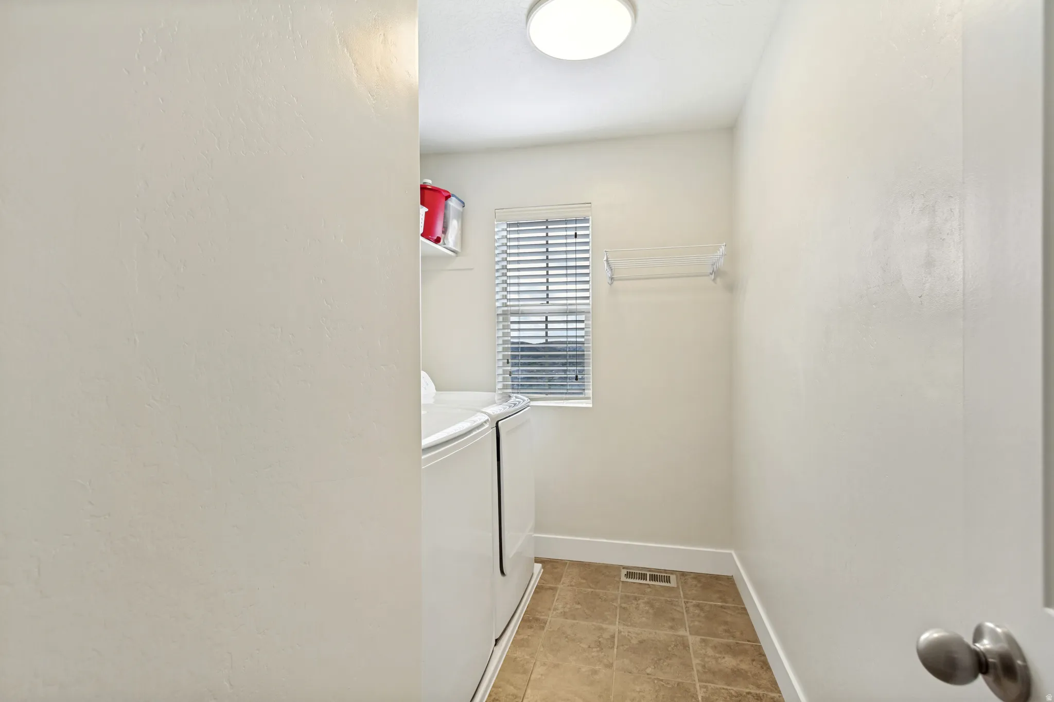 Laundry room featuring tile flooring, a window with blinds, and a ceiling-mounted light fixture
