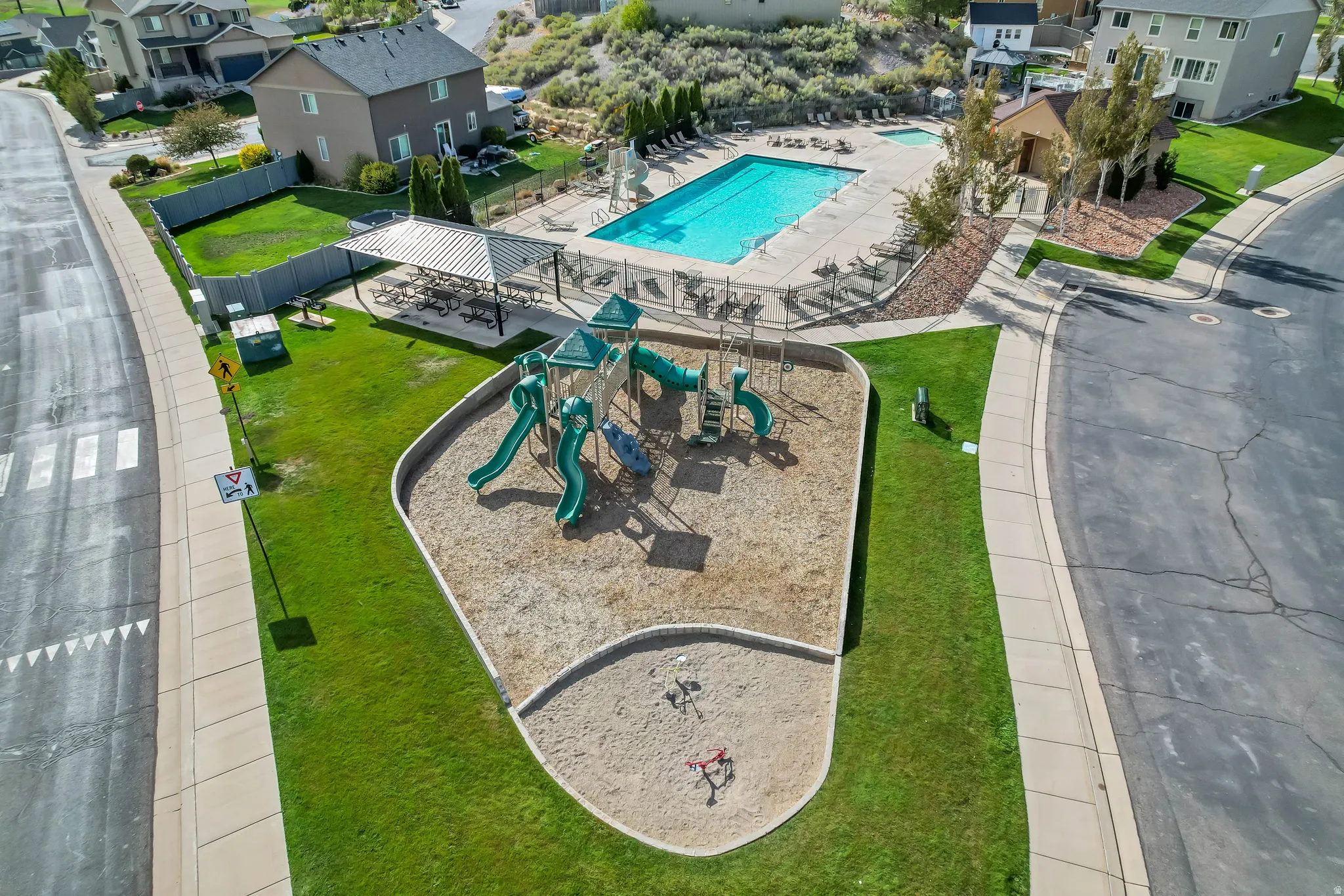 Community playground with multi-level play structure, adjacent to a swimming pool with a paved deck, and a shaded picnic area