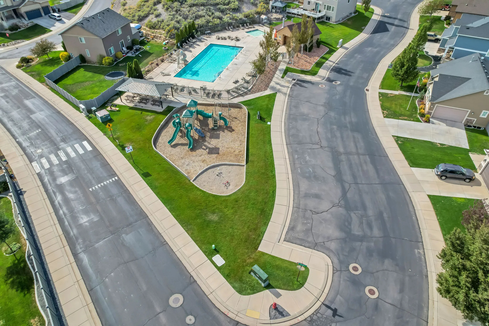 Community amenities featuring a swimming pool, covered outdoor seating, a playground with slides, and a sand area, all surrounded by manicured lawns and paved pathways