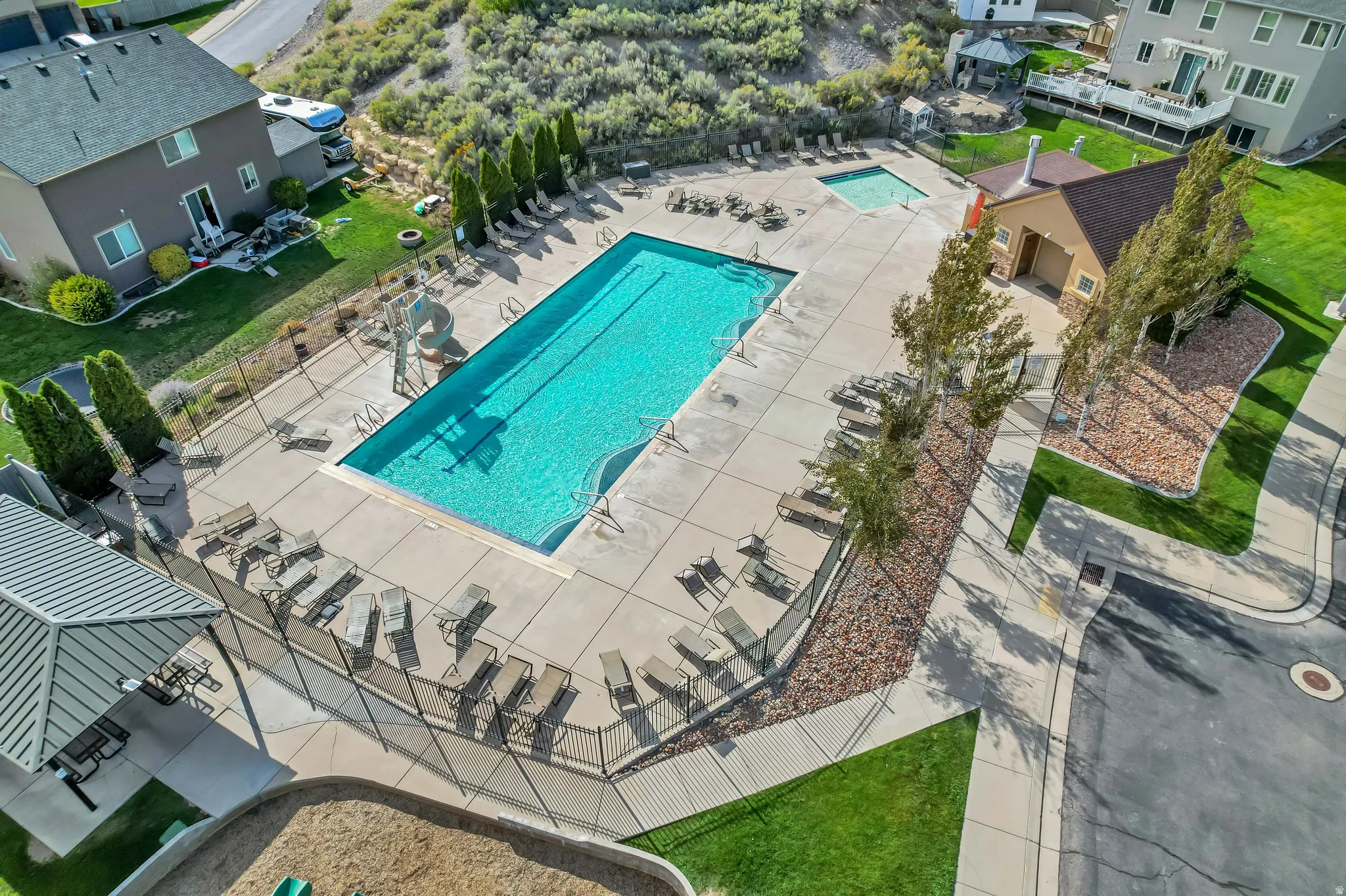 Expansive community pool with a surrounding concrete deck, a separate shallow pool, a shaded picnic area with a metal roof, and an adjacent structure