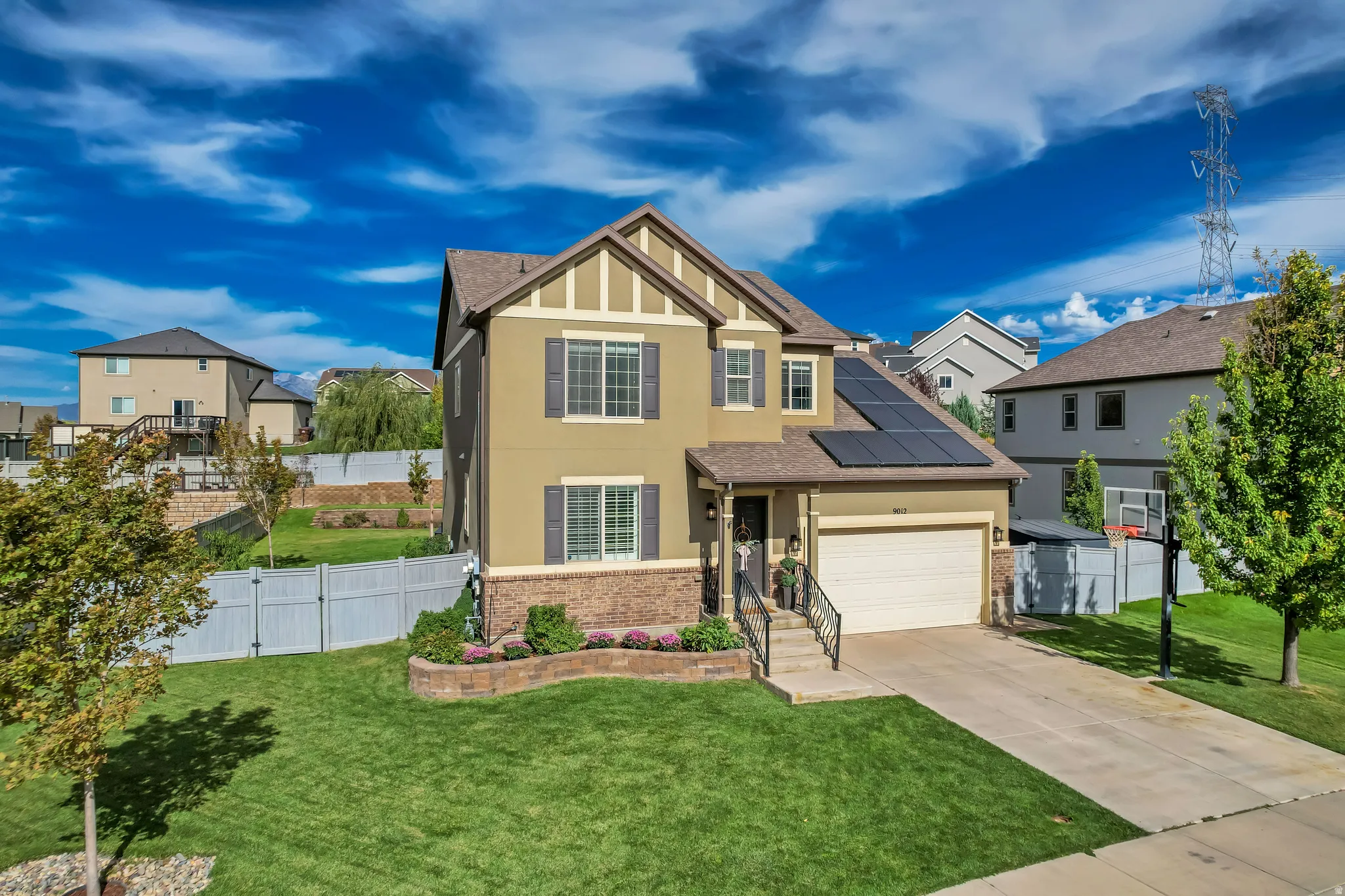 Two-story stucco and stone exterior featuring solar panels, an attached garage, and a concrete driveway