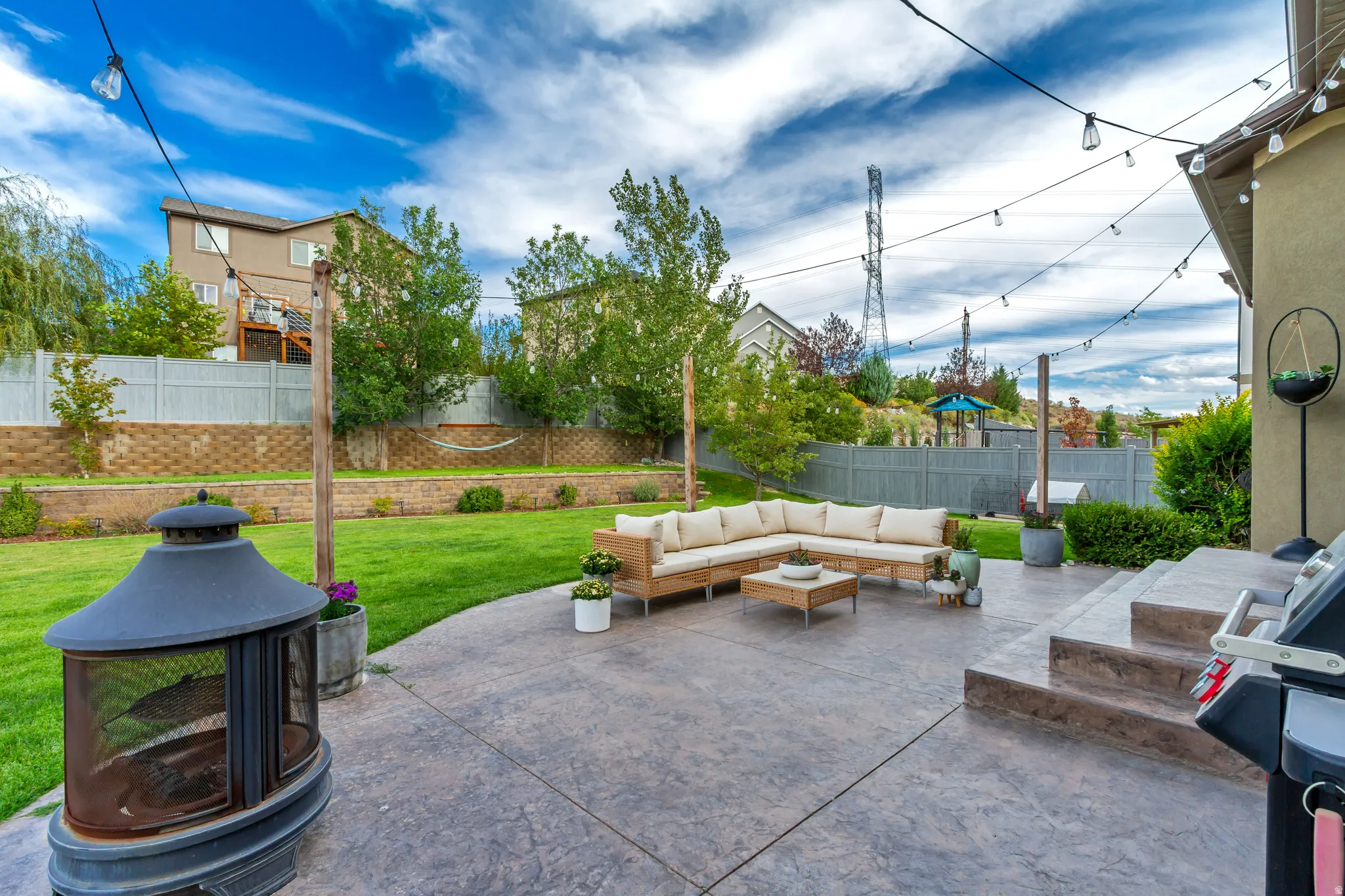 Expansive backyard featuring a stamped concrete patio, tiered steps, a manicured lawn, and retaining walls