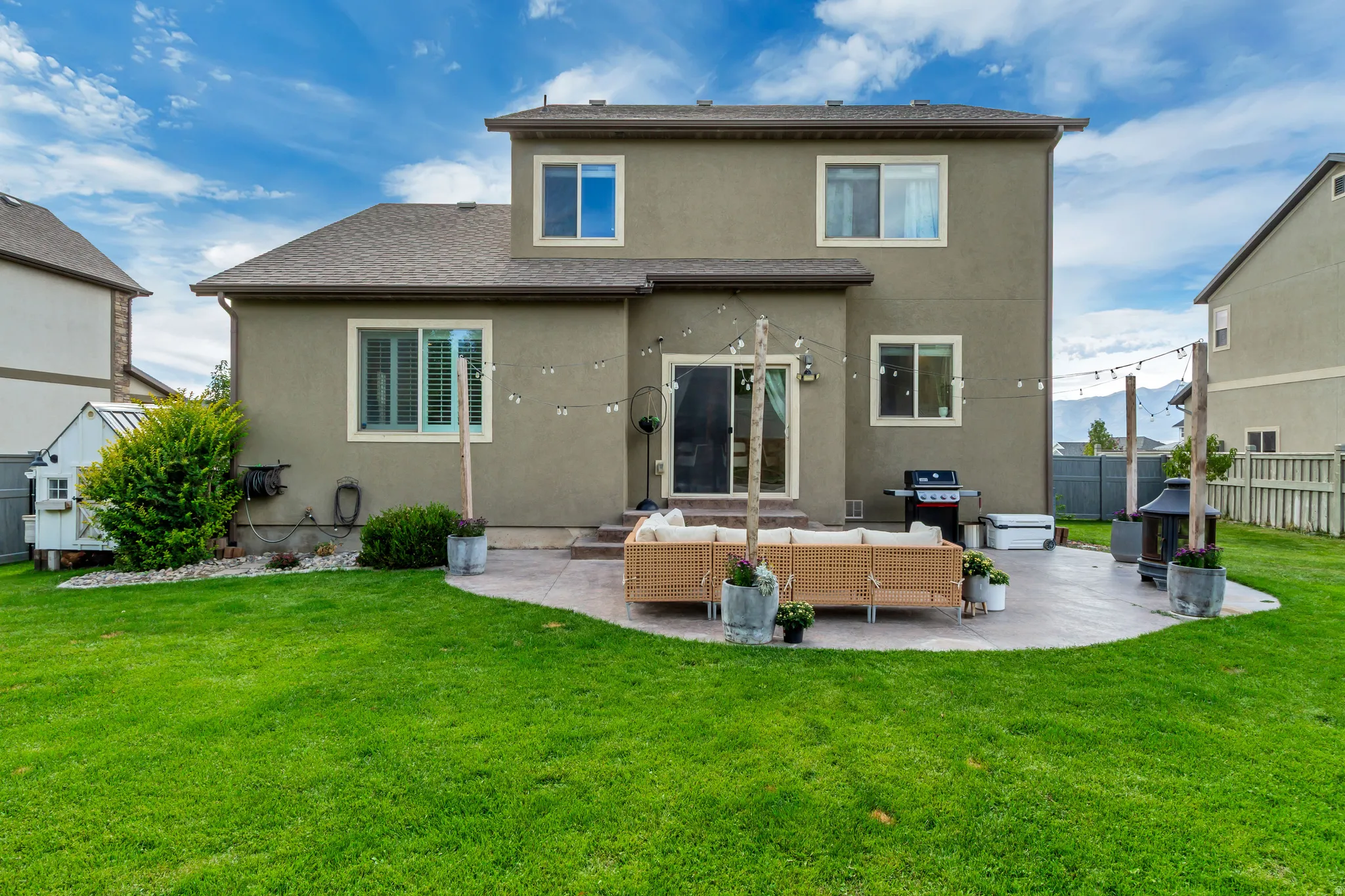 Expansive backyard featuring a manicured lawn, concrete patio, sliding glass door, and multiple windows