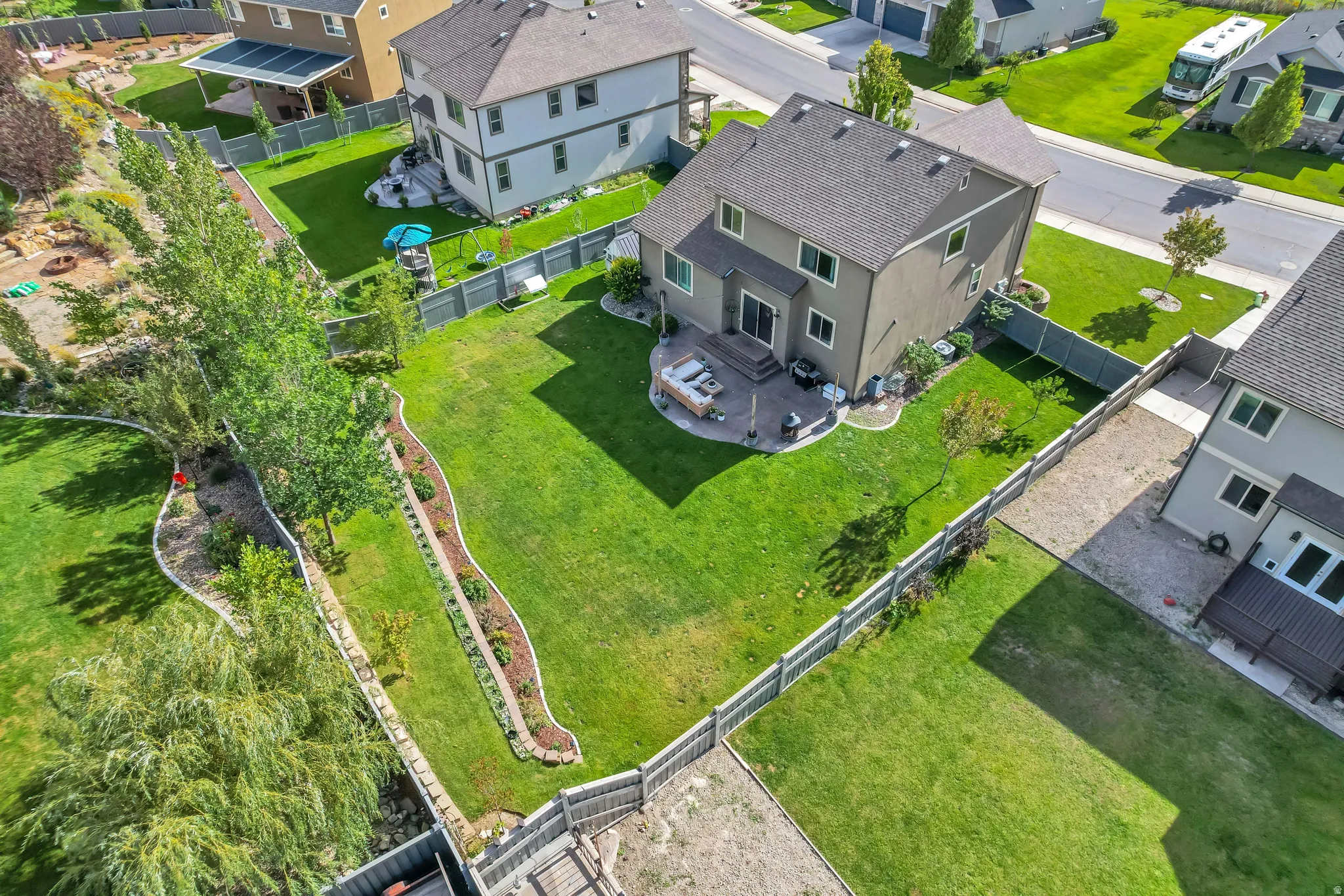 Expansive fenced backyard featuring a manicured lawn, established trees, and a stone patio