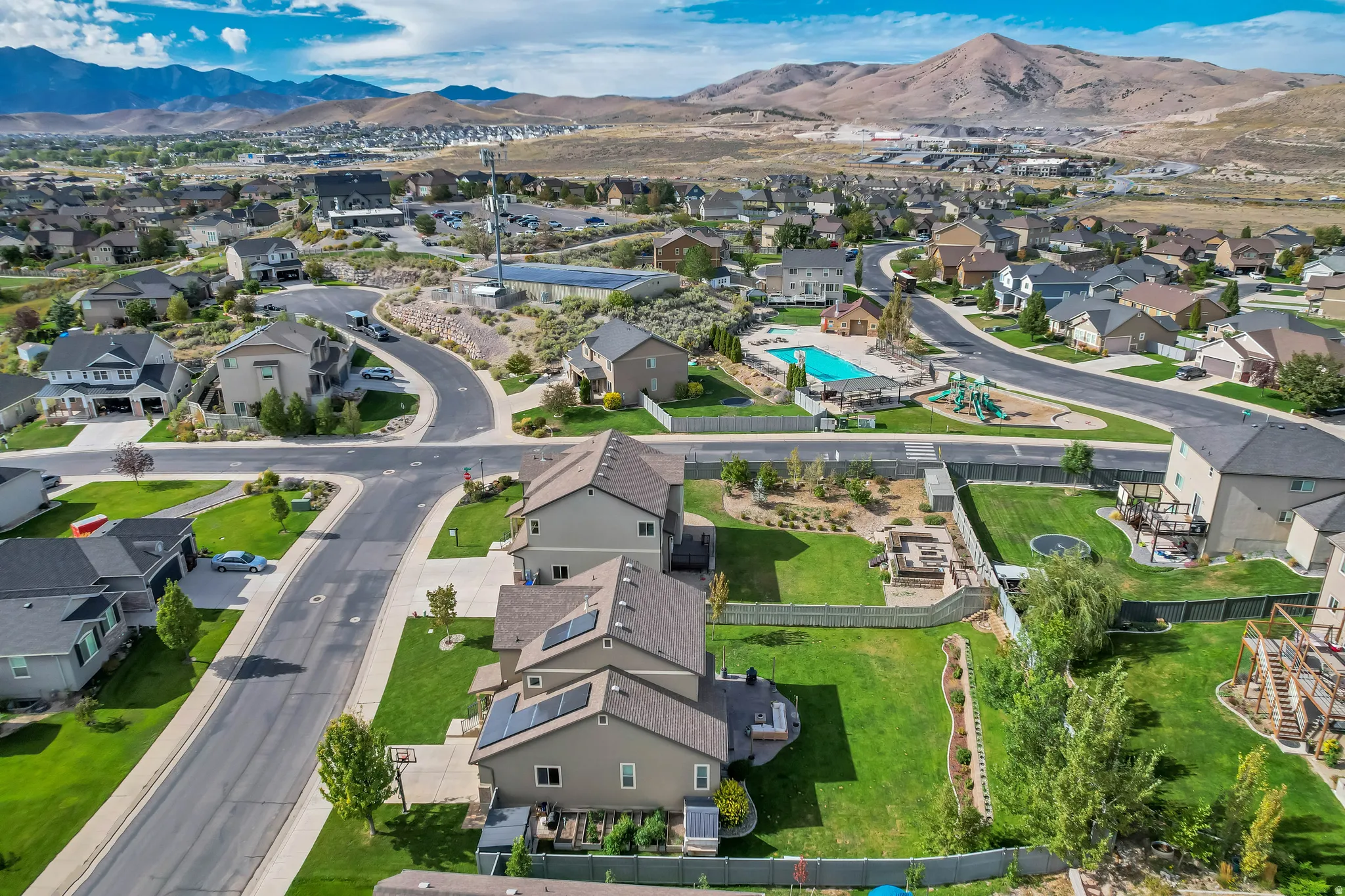 Residential neighborhood with mountain backdrop, featuring a community pool, playground, and paved streets