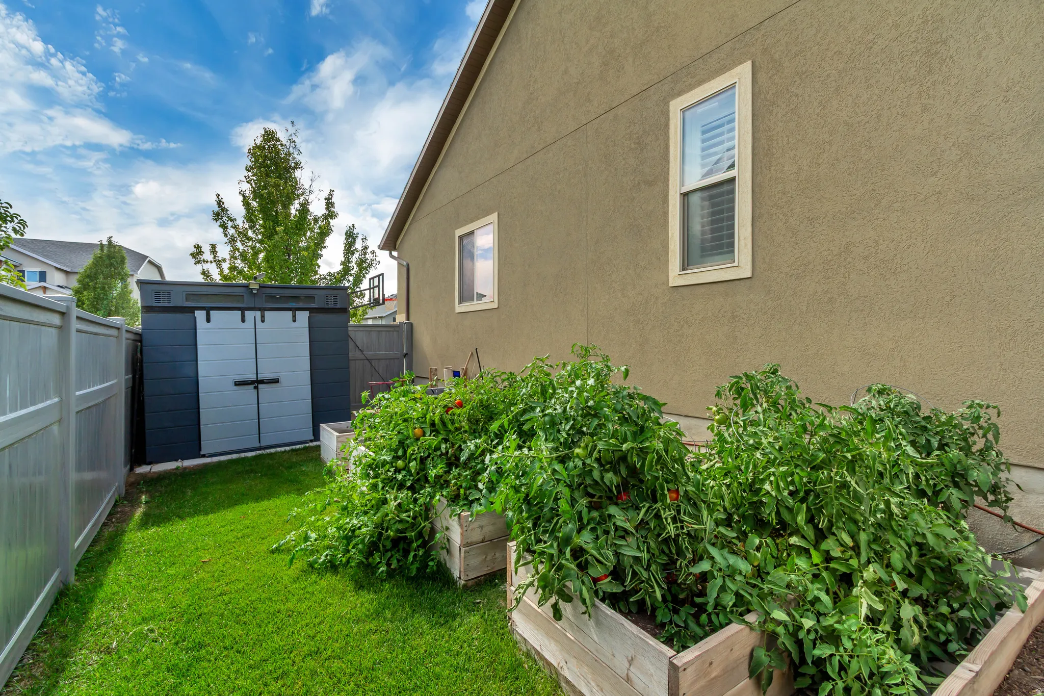 Expansive backyard featuring a manicured lawn, raised garden beds, and a gray privacy fence
