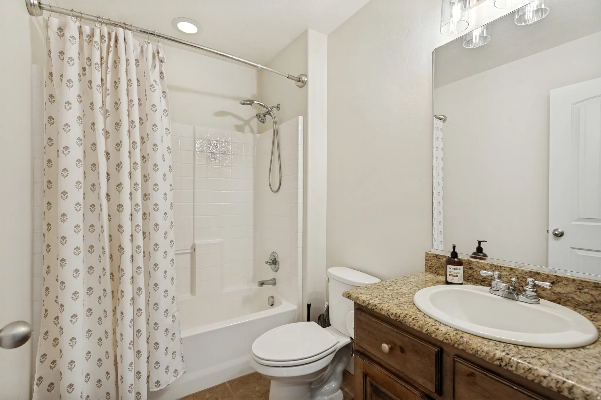 Bathroom featuring a combination shower and tub, white subway tile surround, dark wood-finish vanity with a built-in sink, and a granite-style countertop