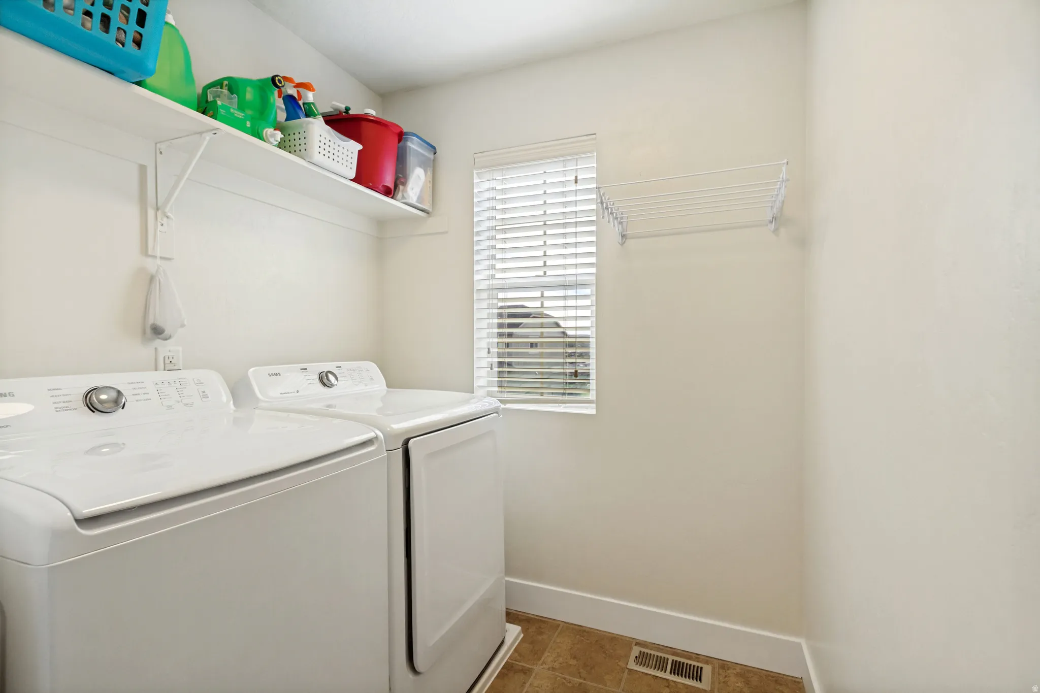 Dedicated laundry area featuring a window with blinds, wall-mounted shelving, and permanent flooring