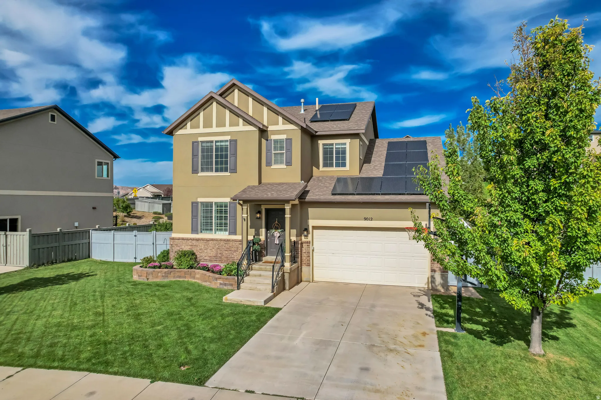 Two-story exterior with stucco and stone accents, featuring solar panels, an attached two-car garage, and a concrete driveway