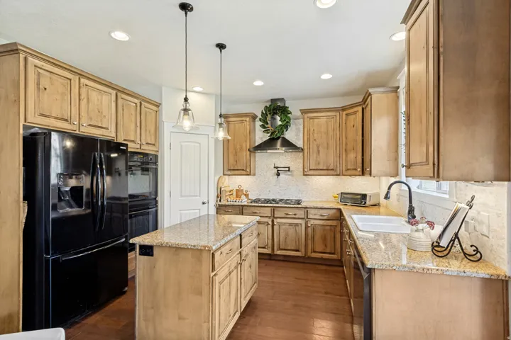 Kitchen featuring wood cabinetry, granite countertops, tile backsplash, a center island, and wood-finish flooring