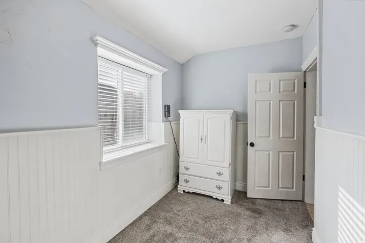 Window with white blinds, white beadboard wainscoting, light gray wall paint, and gray carpet