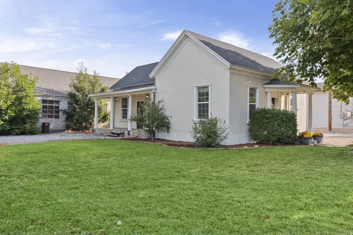 White stucco exterior with a dark shingle roof, featuring a covered porch with pillars