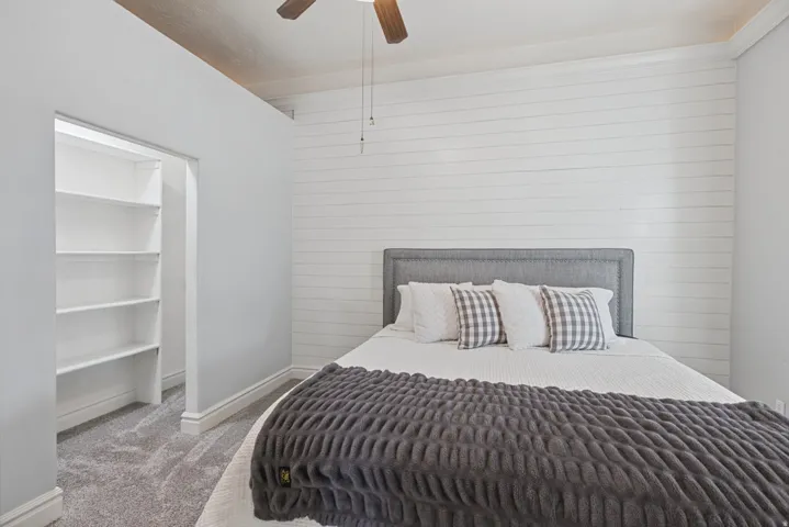 Plank accent wall, wood-finish ceiling fan, built-in shelving, upholstered headboard, and plush carpet flooring