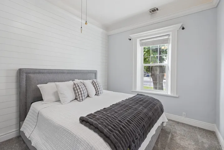 Shapboard accent wall, window with natural light, crown molding, plush carpet flooring, and ceiling-mounted pendant lighting
