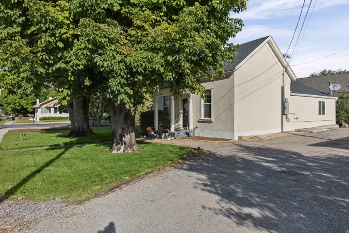 Stucco exterior, gravel driveway, gabled roofline, mature trees, and a manicured lawn