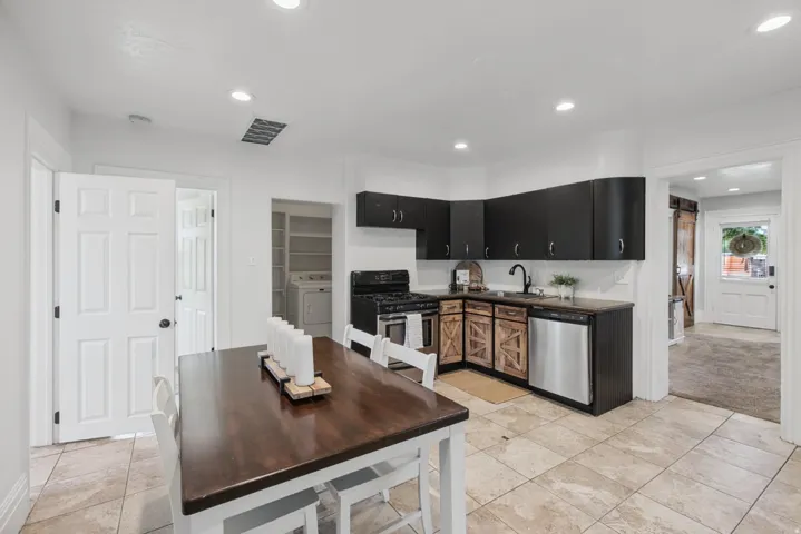 Kitchen featuring dark cabinetry, wood-finish lower cabinets, stainless steel dishwasher, black gas range, and recessed lighting
