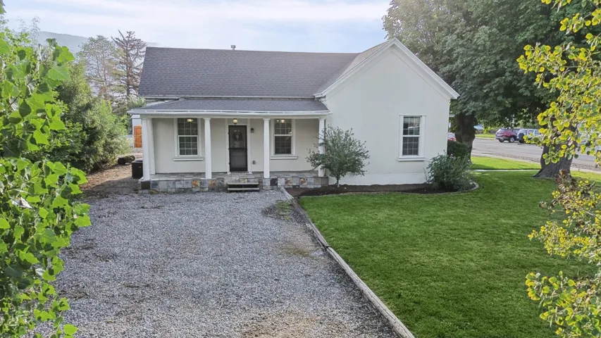 Gable roofline, covered front porch with stone foundation, white exterior facade, gravel driveway, and a manicured front lawn