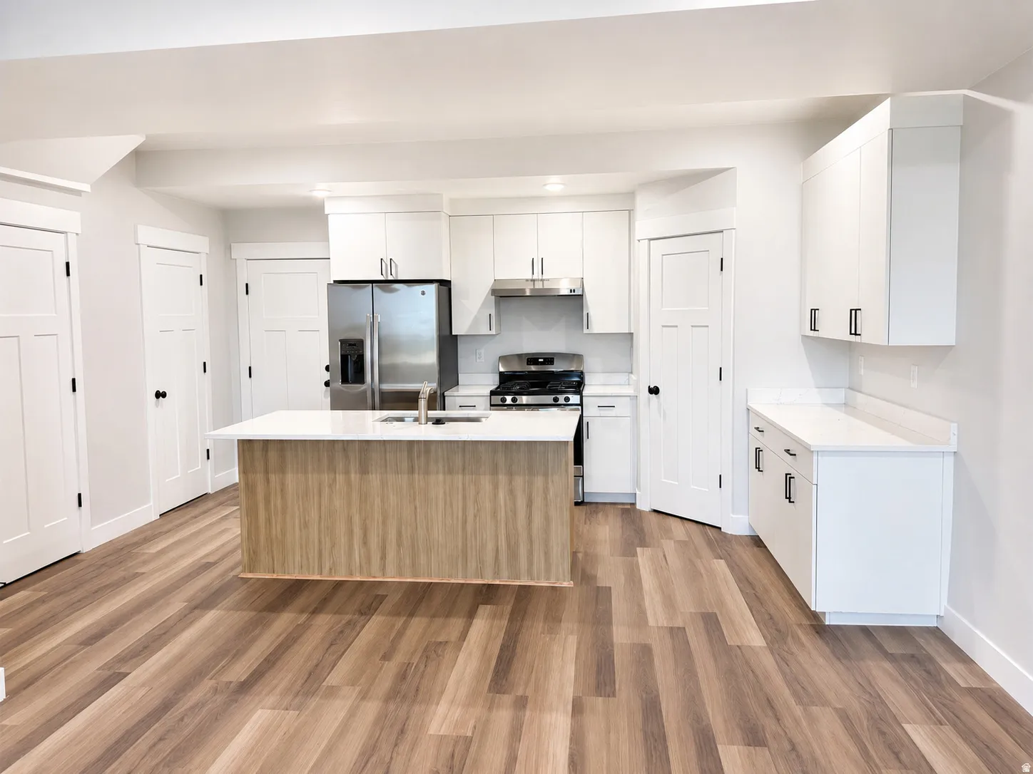 Kitchen featuring a central island with wood-finish paneling, white cabinetry, stainless steel appliances, white countertops, and wood-finish flooring