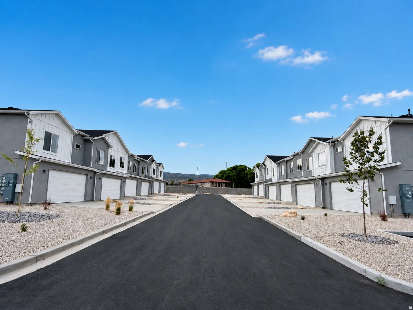 Row of modern townhomes featuring attached garages, dark asphalt driveway, and gravel landscaping