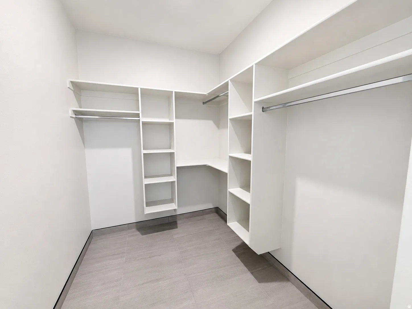 Built-in white shelving system, multiple hanging rods, and gray tile flooring