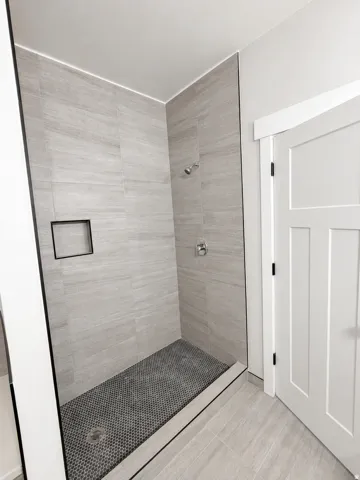 Walk-in shower with large format tile walls, black penny tile shower floor, and a built-in shower niche