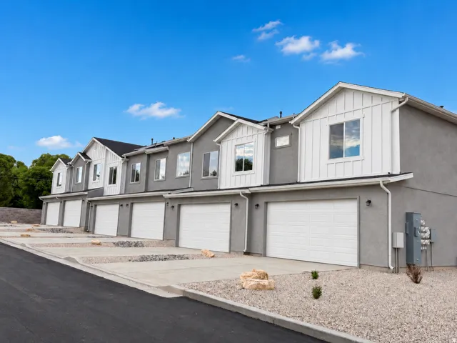 Row of residential units featuring stucco exteriors, white board-and-batten gables, attached garages, and a gravel landscape