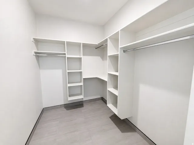 Built-in white shelving system, multiple hanging rods, and gray tile flooring