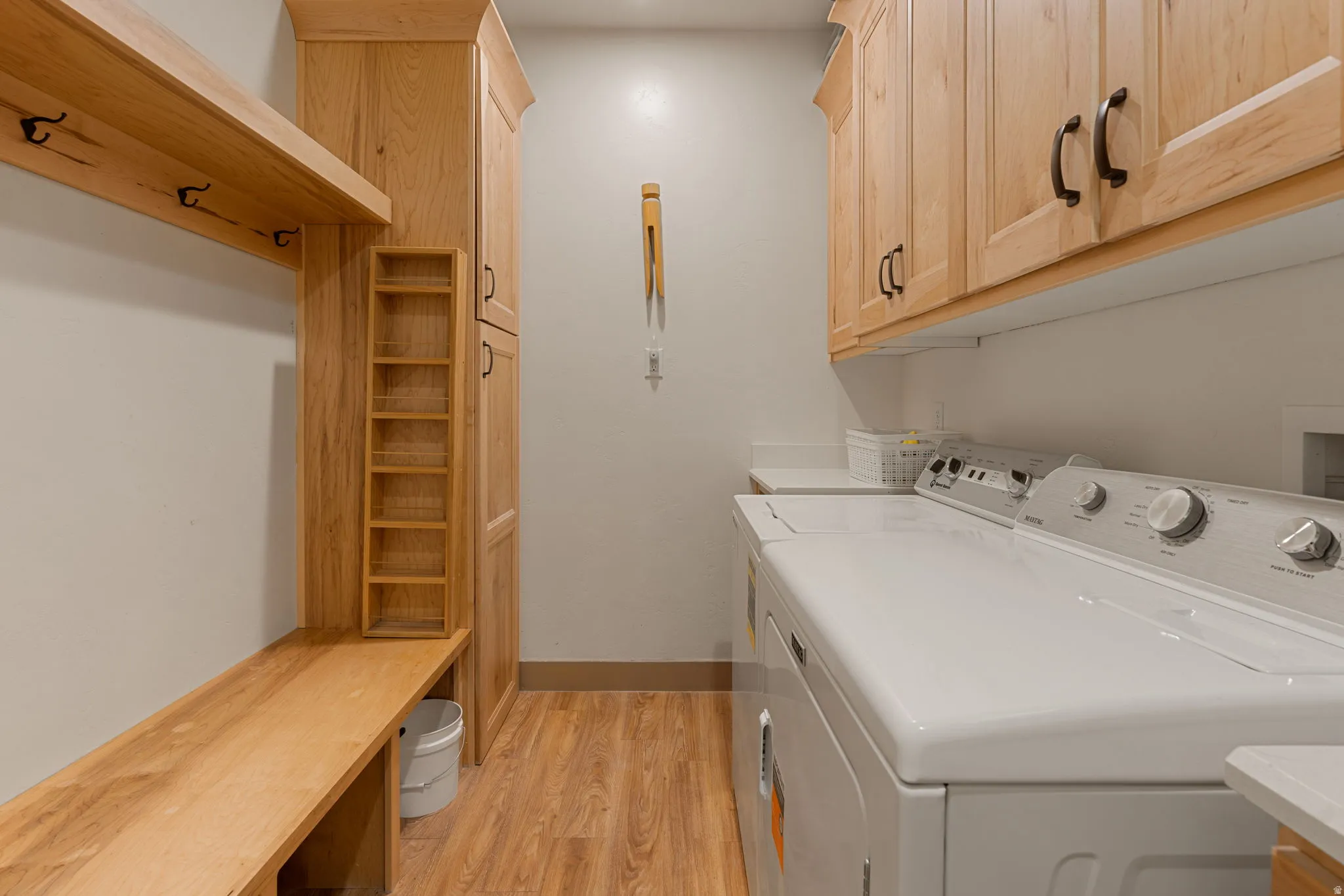 Built-in wooden bench with coat hooks, full-height wooden cabinetry, upper wooden cabinetry, and wood-finish flooring