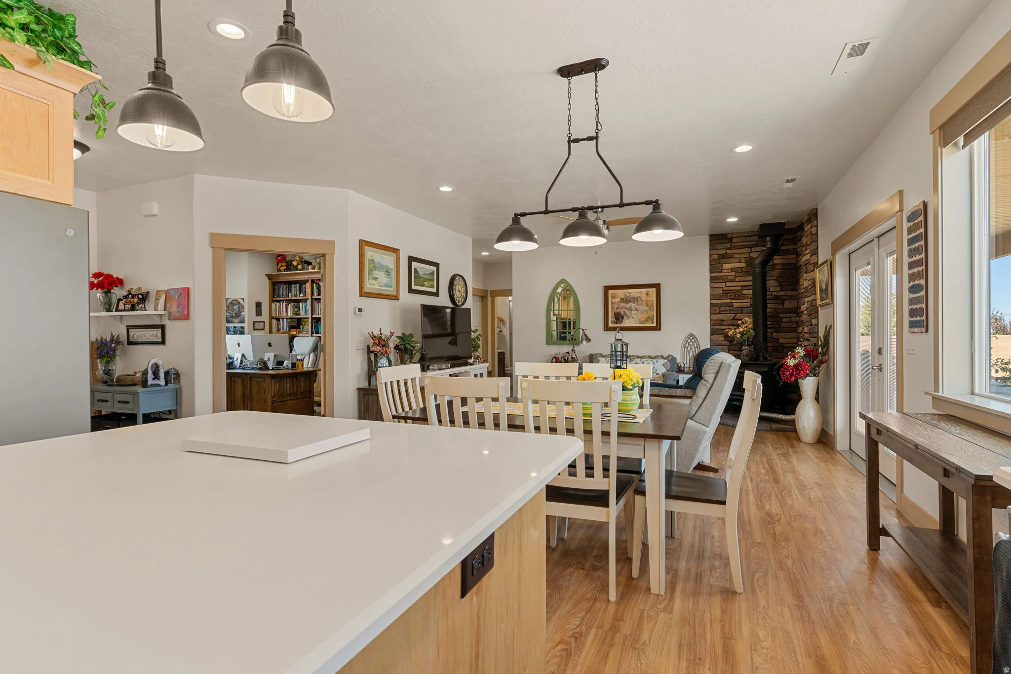 Spacious open-concept living area featuring a stone accent wall, wood-finish flooring, and ample natural light from large windows