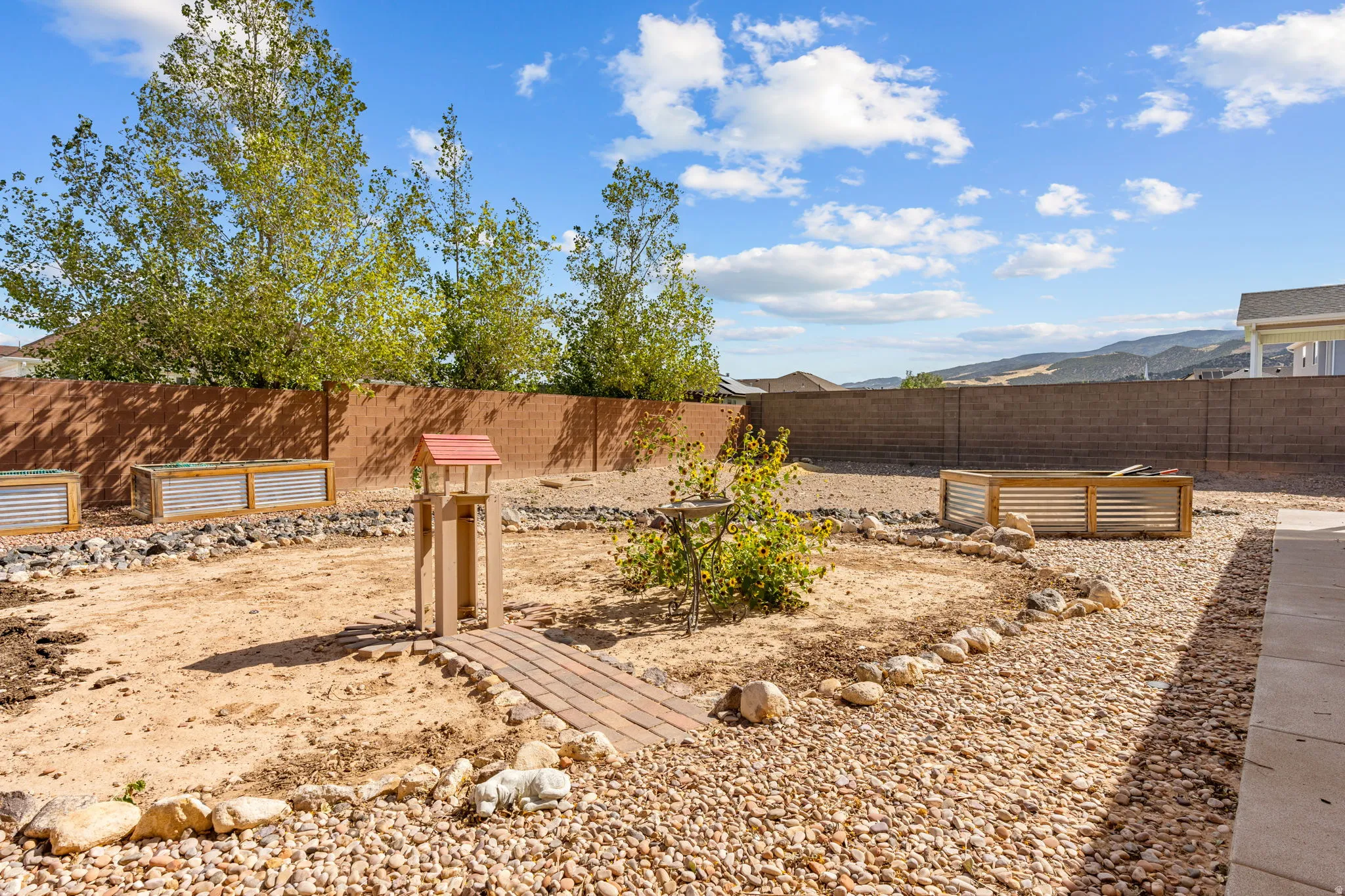Expansive backyard featuring a concrete block fence, raised garden beds, a gravel pathway, and a patio area