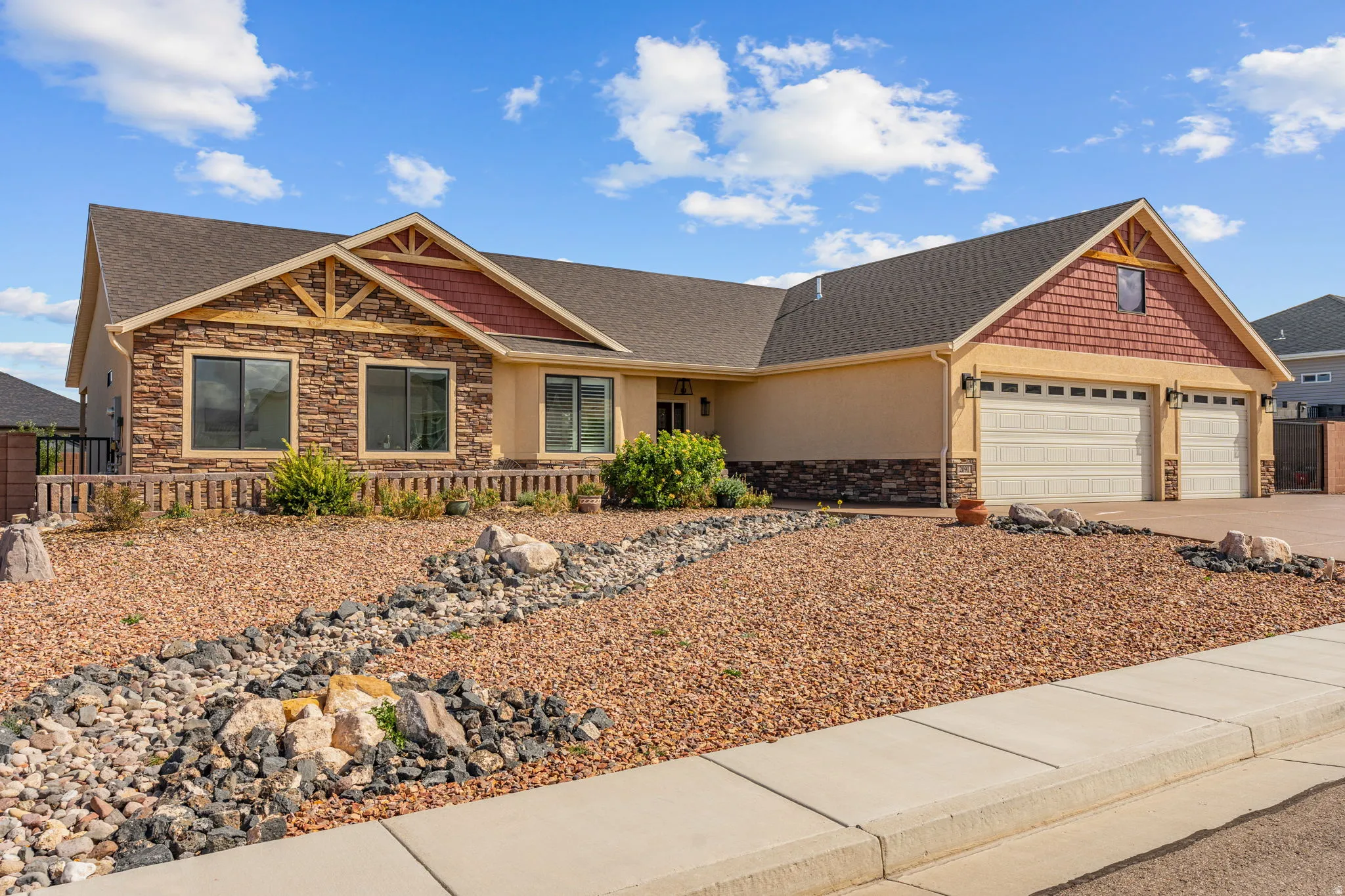 Stucco and stone facade with gabled roof lines, two-car garage, and xeriscaped front yard