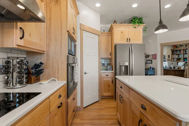 Kitchen featuring light wood cabinetry, a stainless steel refrigerator, a built-in oven, a cooktop, and an expansive island with a light-toned countertop