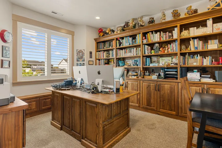 Built-in wood cabinetry with integrated shelving, wood-finish desk, and window with plantation shutters