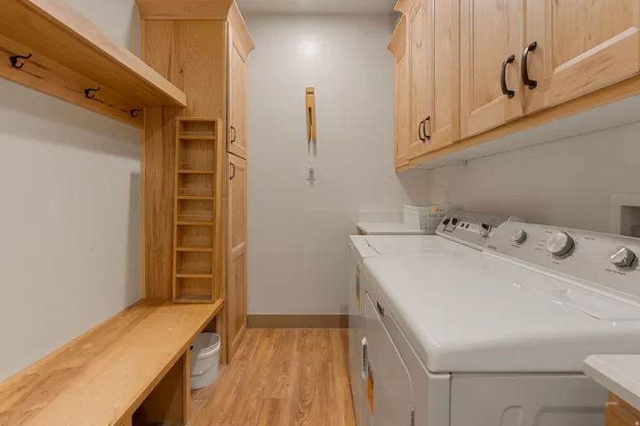 Built-in wooden bench with coat hooks, full-height wooden cabinetry, upper wooden cabinetry, and wood-finish flooring