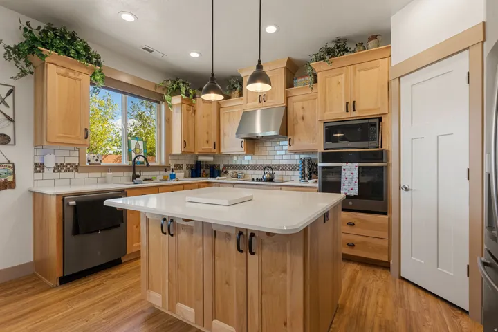 Kitchen featuring wood-finish flooring, light wood cabinetry, a center island with a light countertop, stainless steel appliances, and a tile backsplash