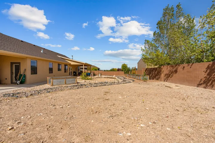 Expansive backyard area with a covered patio, raised garden beds, and a perimeter wall