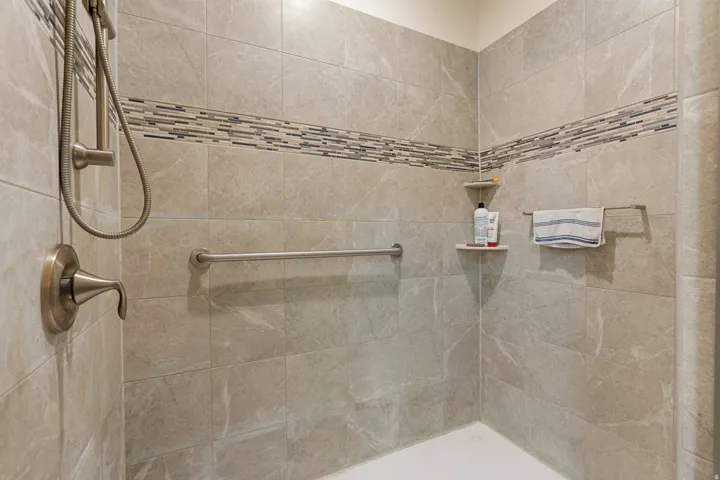 Tiled shower with a mosaic accent band, brushed nickel fixtures, and built-in corner shelving