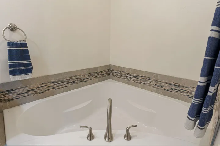 Corner soaking tub with brushed nickel fixtures and a mosaic tile surround