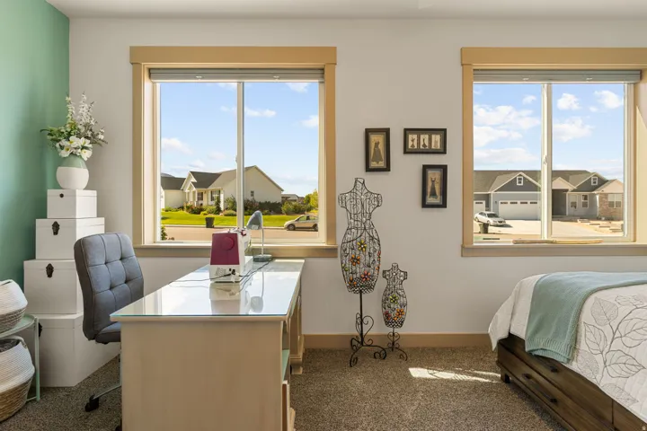 Carpeted flooring, dual windows with wood-finish trim, and a built-in desk with a glass top