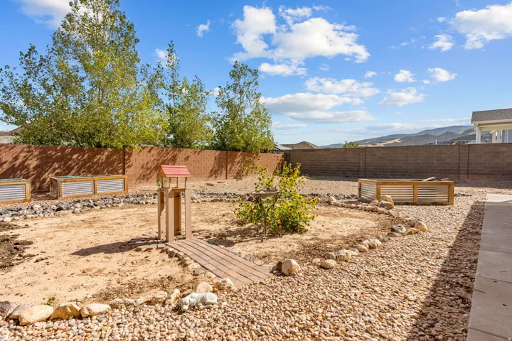 Expansive backyard featuring a concrete block fence, raised garden beds, a gravel pathway, and a patio area