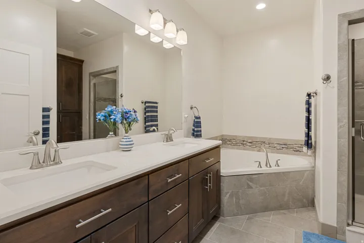 Dual vanity with integrated sinks, brushed nickel fixtures, built-in soaking tub, tile flooring, and glass-enclosed shower