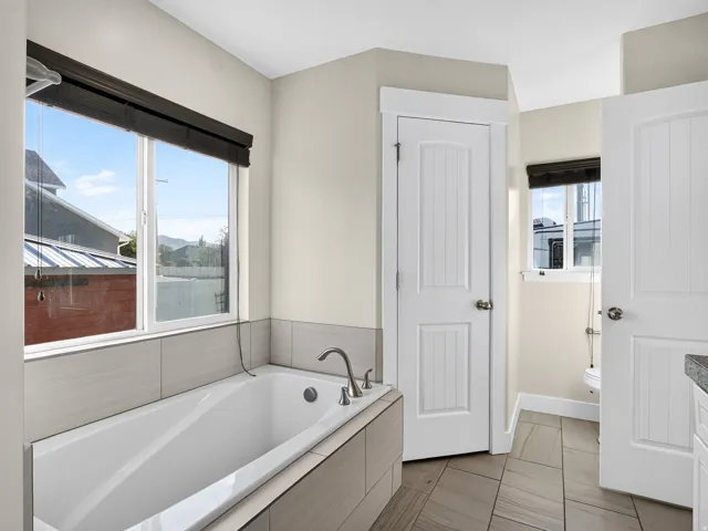 Soaking tub with brushed nickel fixtures, tile surround, and a large window