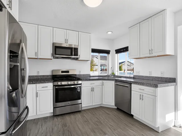 Kitchen featuring stainless steel appliances, white cabinetry, dark speckled countertops, and wood-finish flooring