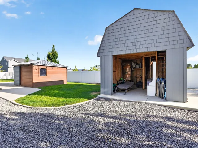 Gravel driveway leading to a concrete pad, a shed with wood-finish siding, and a second outbuilding featuring shingle siding
