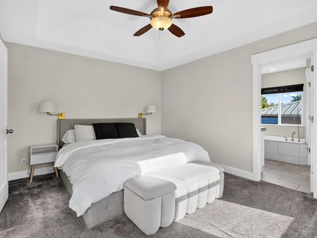 Tray ceiling with a ceiling fan, wall-mounted sconce lighting, and soft gray carpeting