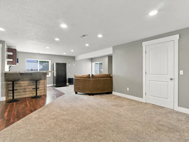 Recessed lighting, wood-finish flooring, built-in bar with stone-look countertop, board and batten interior door, and neutral-toned carpeting