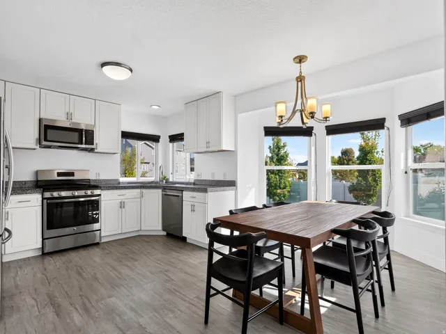 Kitchen featuring white cabinetry, stainless steel appliances, wood-finish flooring, and a dining area with a chandelier