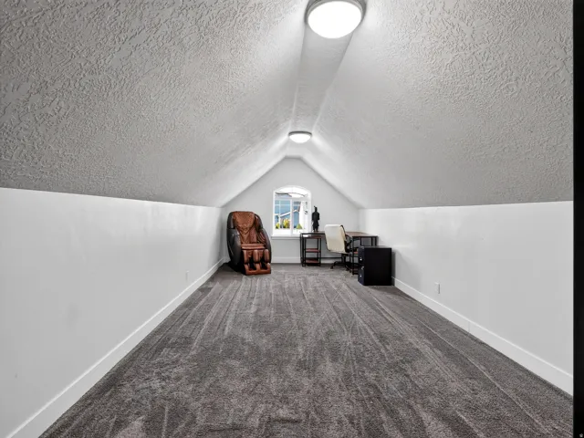 Carpeted attic space featuring white walls and a window