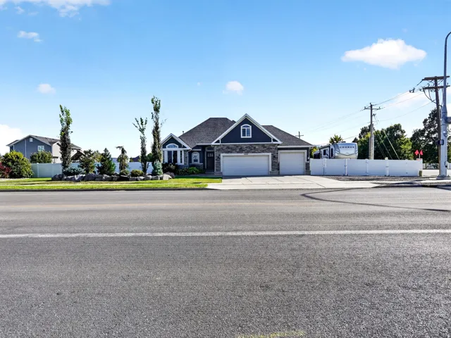 Spacious residence featuring a two-car garage, stone and siding exterior, front yard landscaping with mature trees, and a white privacy fence