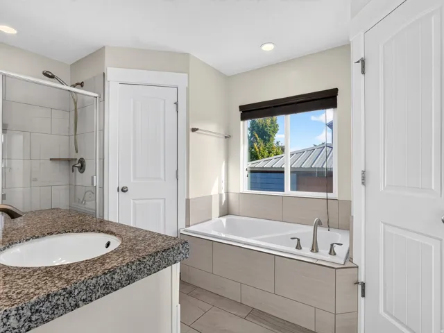 Granite-finish vanity countertop with an undermount sink, built-in bathtub with tile surround, glass-enclosed shower with tiled walls, and recessed lighting
